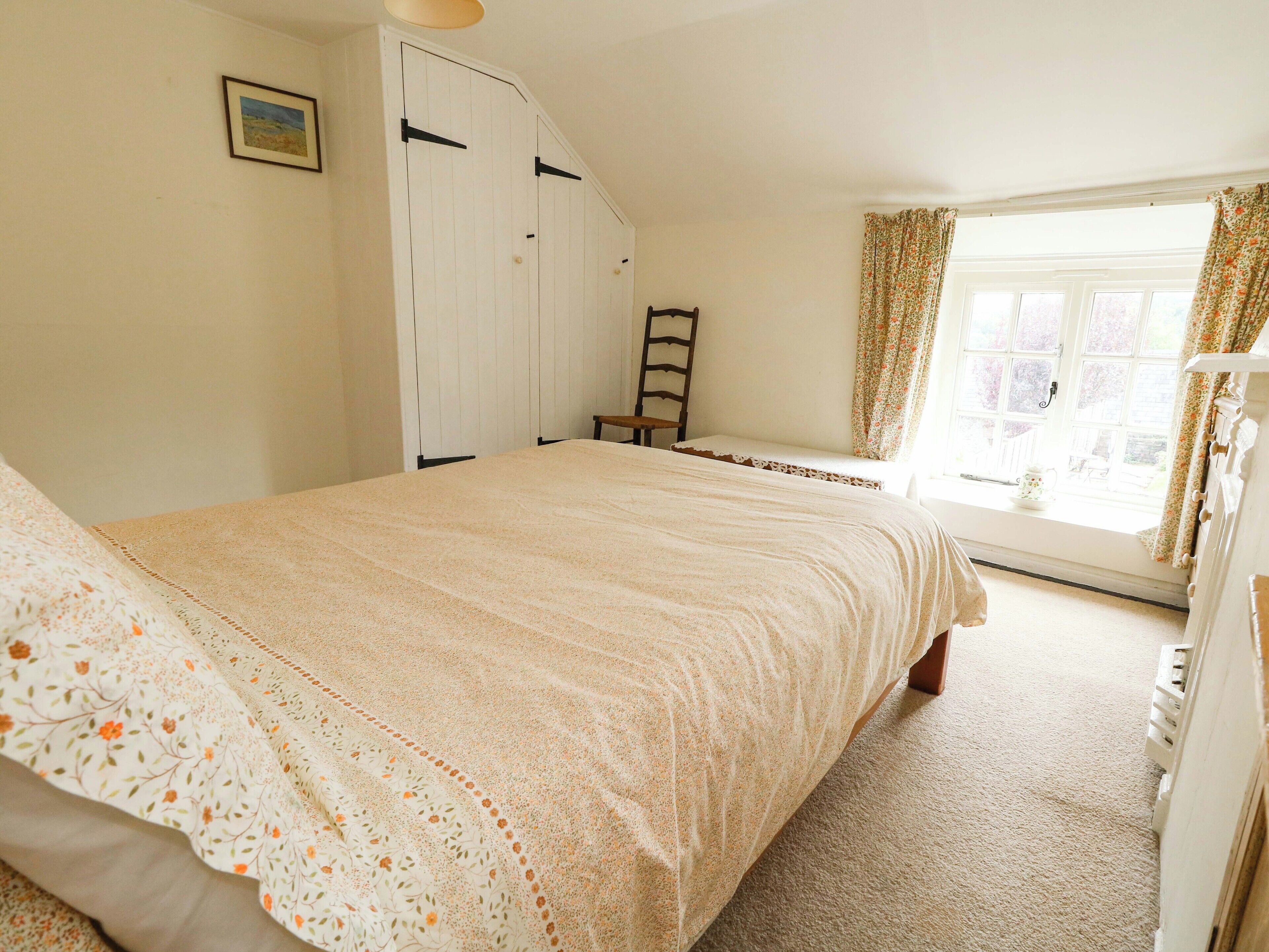 A bedroom with a large bed, a window with curtains, a wardrobe, and a chair.