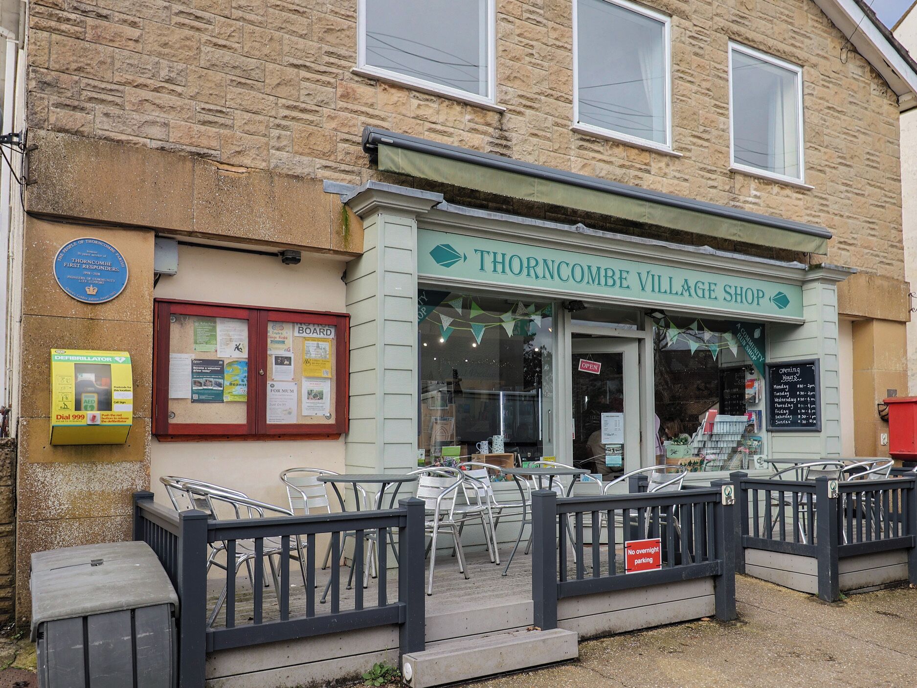A storefront with a sign reading "Thorncombe Village Shop" and a "No overnight parking" sign.