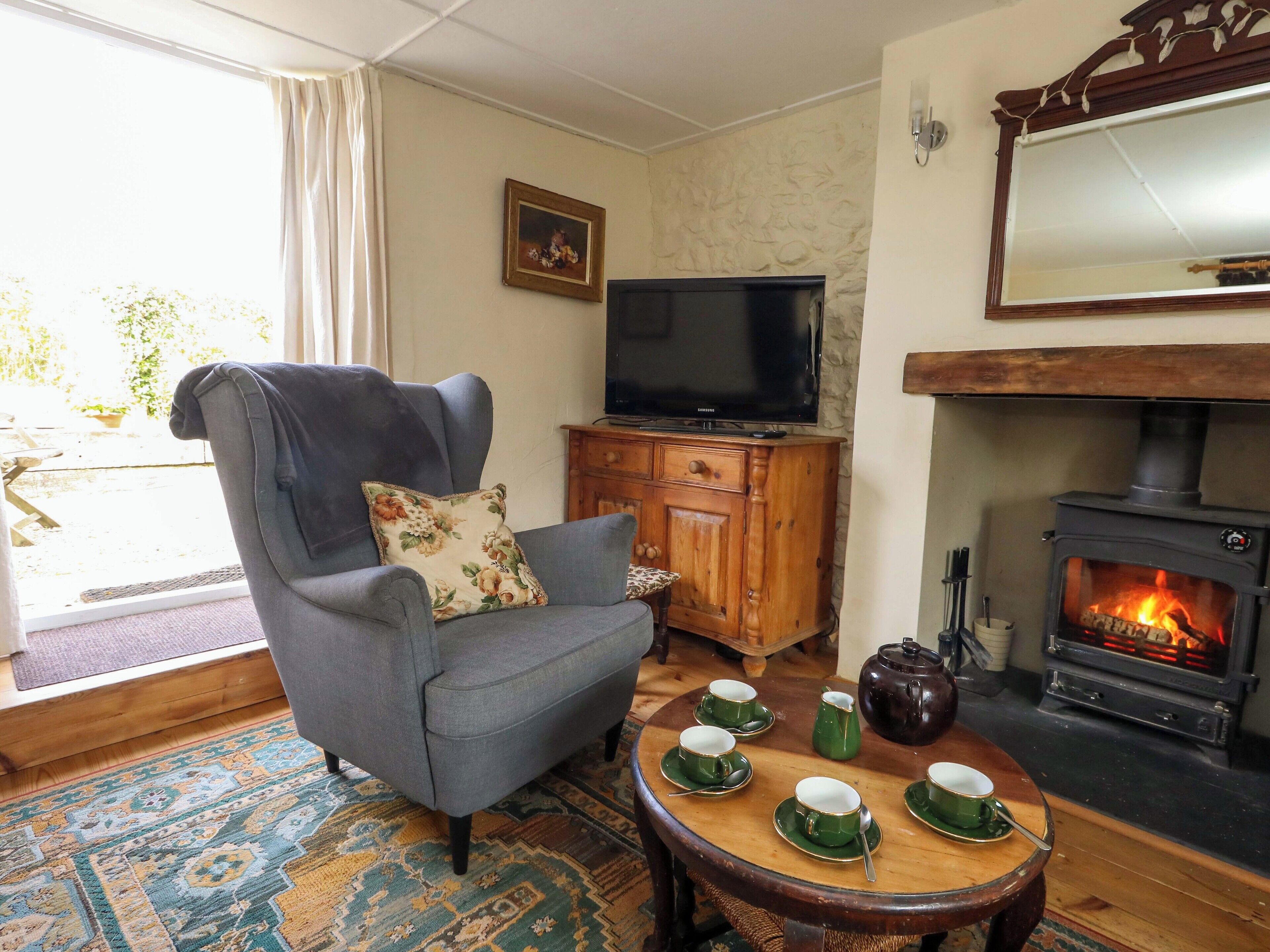 A living room with a grey armchair, a television, a wooden cabinet, a fireplace, and a table with green cups and saucers.