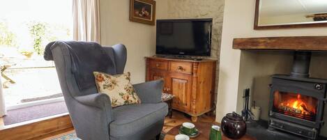 A living room with a grey armchair, a television, a wooden cabinet, a fireplace, and a table with green cups and saucers.