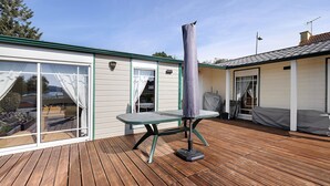 Une terrasse en bois avec une table et un objet couvert, un bâtiment doté de grandes fenêtres et d’un patio abrité.