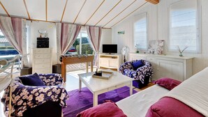 Une pièce confortable avec un canapé, une petite table, un téléviseur et une fenêtre donnant sur l’extérieur.