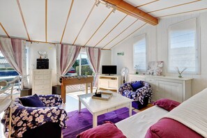 Et hyggeligt værelse med en sofa, et lille bord, et fjernsyn og et vindue med udsigt.