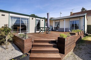 Une maison à deux étages dotée d’une terrasse en bois, d’un patio et d’un jardin avec des plates-bandes surélevées.