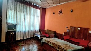 Una habitación con una cama, cabecera de madera, una mesita, un televisor y una ventana con cortinas.