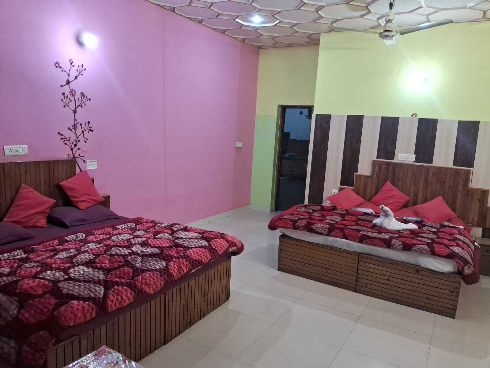 A bedroom with two beds, each with a wooden headboard and red bedding. The room has a pink wall and a ceiling with a hexagonal pattern.