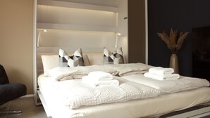 A neatly made bed with white linens and pillows, a bedside lamp, and a vase with dried plants on the nightstand. - Stylish living - job & vacation (Soltau)