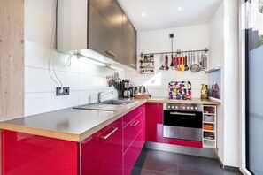 Una cocina moderna con armarios rojos, electrodomésticos de acero inoxidable y una variedad de utensilios colgando en la pared.