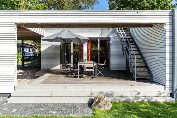Un patio techado al aire libre con una mesa, sillas, una escalera y vistas del vecindario.