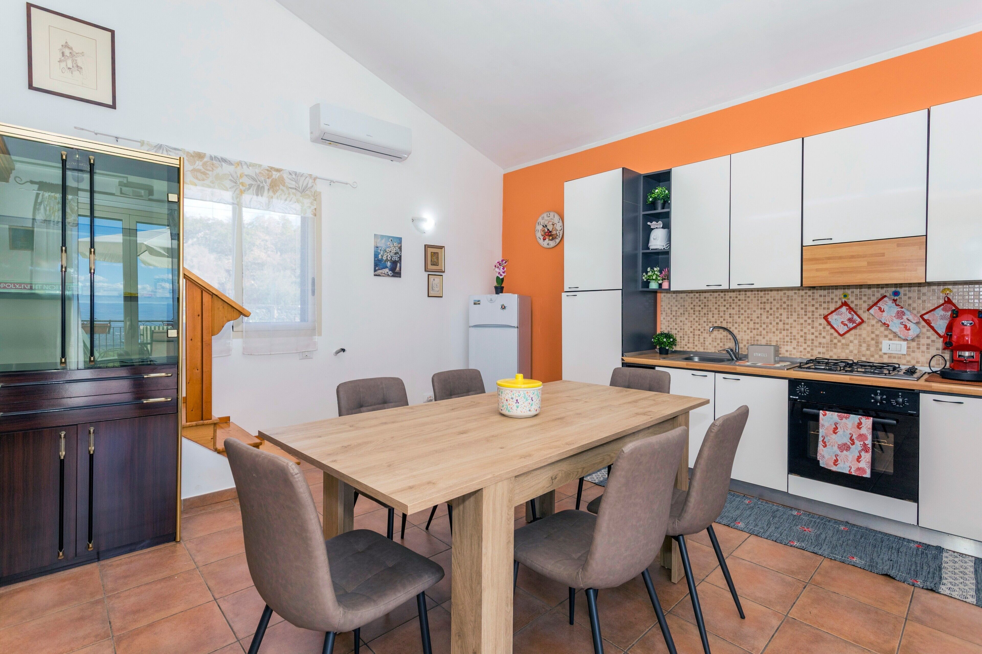A modern kitchen with white cabinets, a wooden dining table, and a built-in oven.