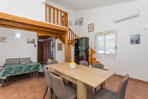 Un espace repas avec une table et des chaises en bois, un escalier et un coin cuisine.