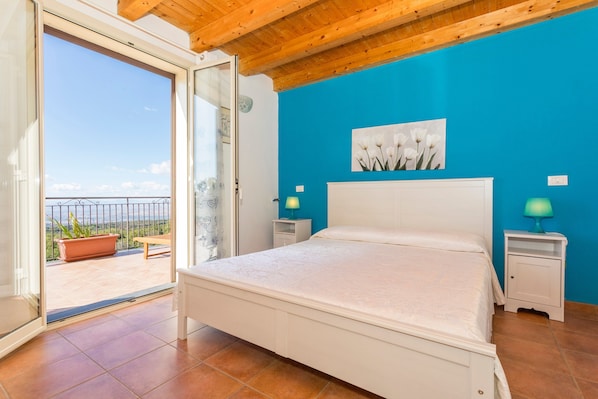 Une chambre avec un lit, un balcon offrant une vue et un mur bleu.