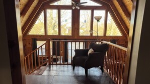 A wooden cabin with a balcony, a ceiling fan, and a chair with a cushion. - Riverfront 2-bedroom house tons of light, AC, deck & patio Sleeps 8 Pet Friendly (Fort Edward)
