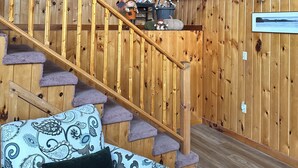 A wooden interior with a staircase, a sofa with patterned cushions, and a framed picture on the wall. - Riverfront 2-bedroom house tons of light, AC, deck & patio Sleeps 8 Pet Friendly (Fort Edward)