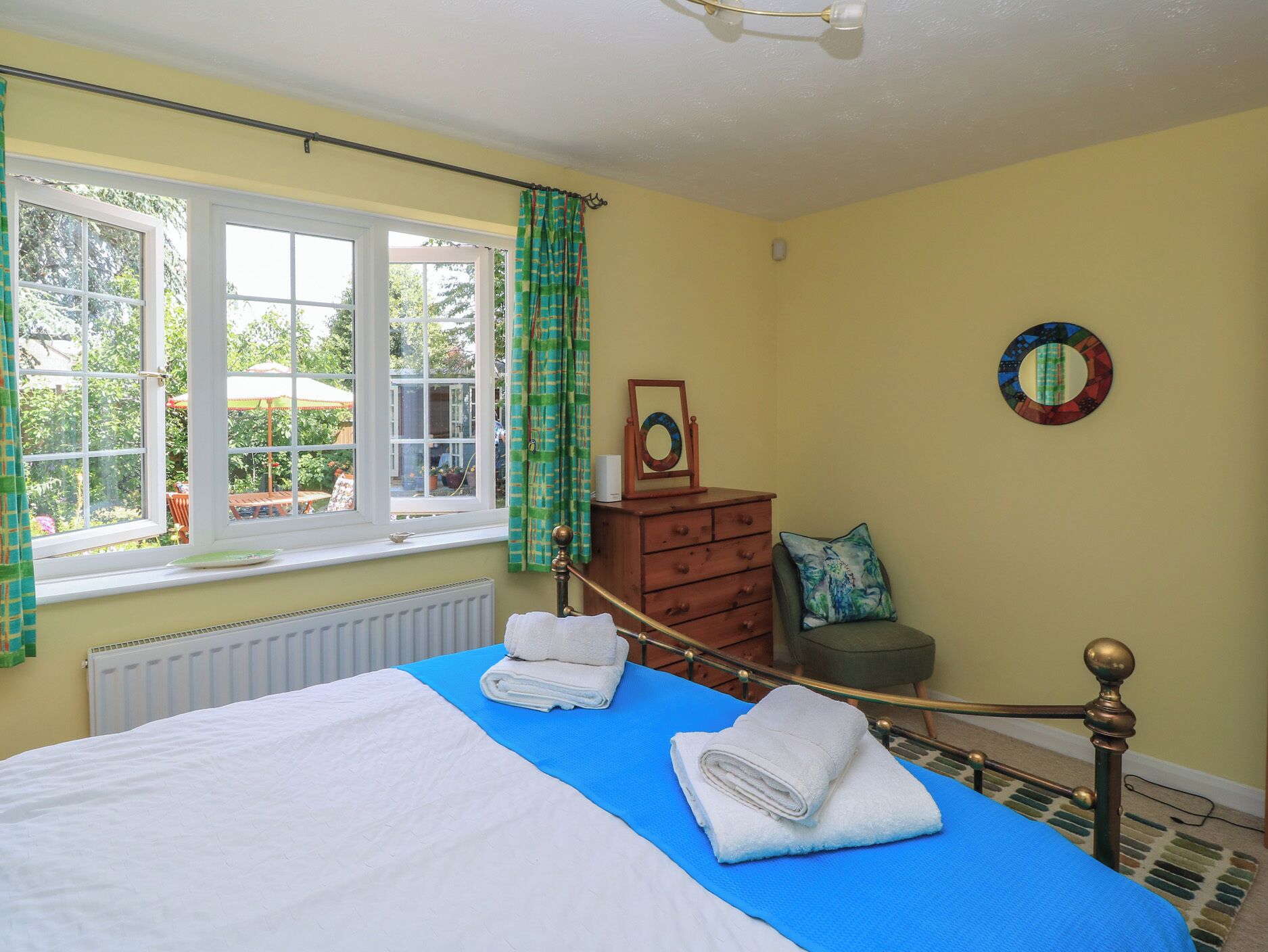 A bedroom with a bed, a dresser, a mirror, and a view of the outdoors through a window.