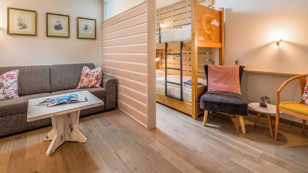 Een moderne kamer met een bank, een klein tafeltje met een tijdschrift, een stapelbed, een stoel en een klein tafeltje met een plant.