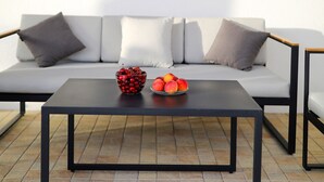 A modern outdoor seating area with a black table, white sofa, and grey shutters on a window.