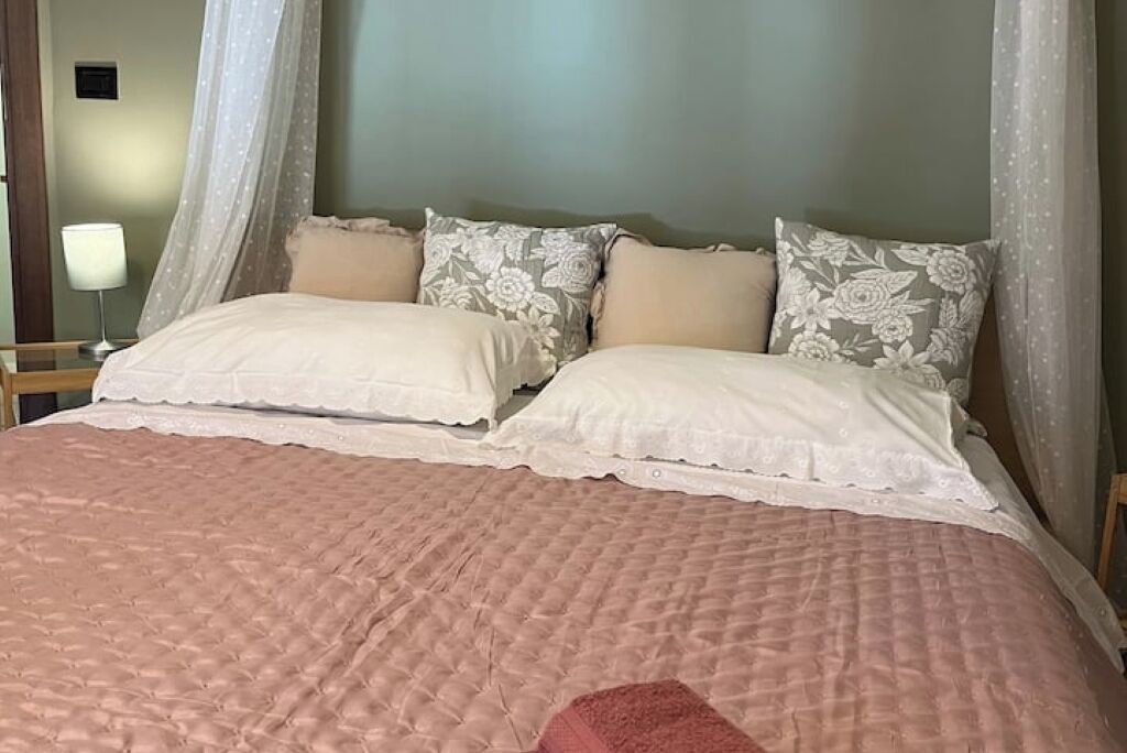 Un lit recouvert d’une courtepointe rose à motifs matelassés, deux oreillers blancs ornés de motifs floraux et un baldaquin agrémenté de rideaux transparents.