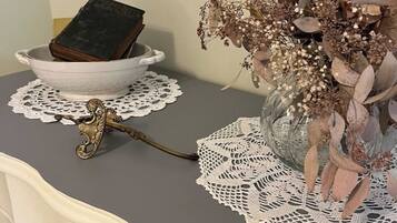 Una mesa con un cuenco blanco que contiene un libro, un mantel de encaje, un florero con flores secas y un objeto metálico decorativo.