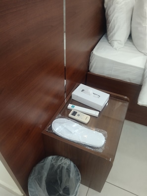 Une table de chevet en bois avec une télécommande, une boîte de mouchoirs et un objet emballé dans du plastique.