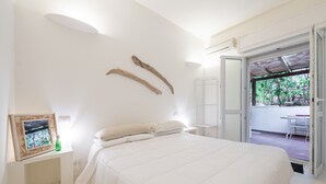 Un dormitorio con cama, una mesita de noche con un cuadro enmarcado y vistas a un espacio exterior.
