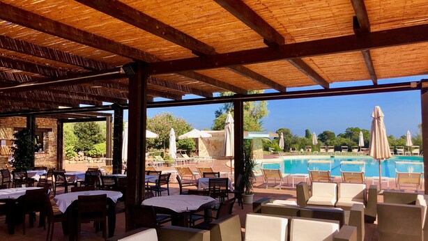 Un espacio al aire libre con mesas y sillas, una piscina y vistas del paisaje.