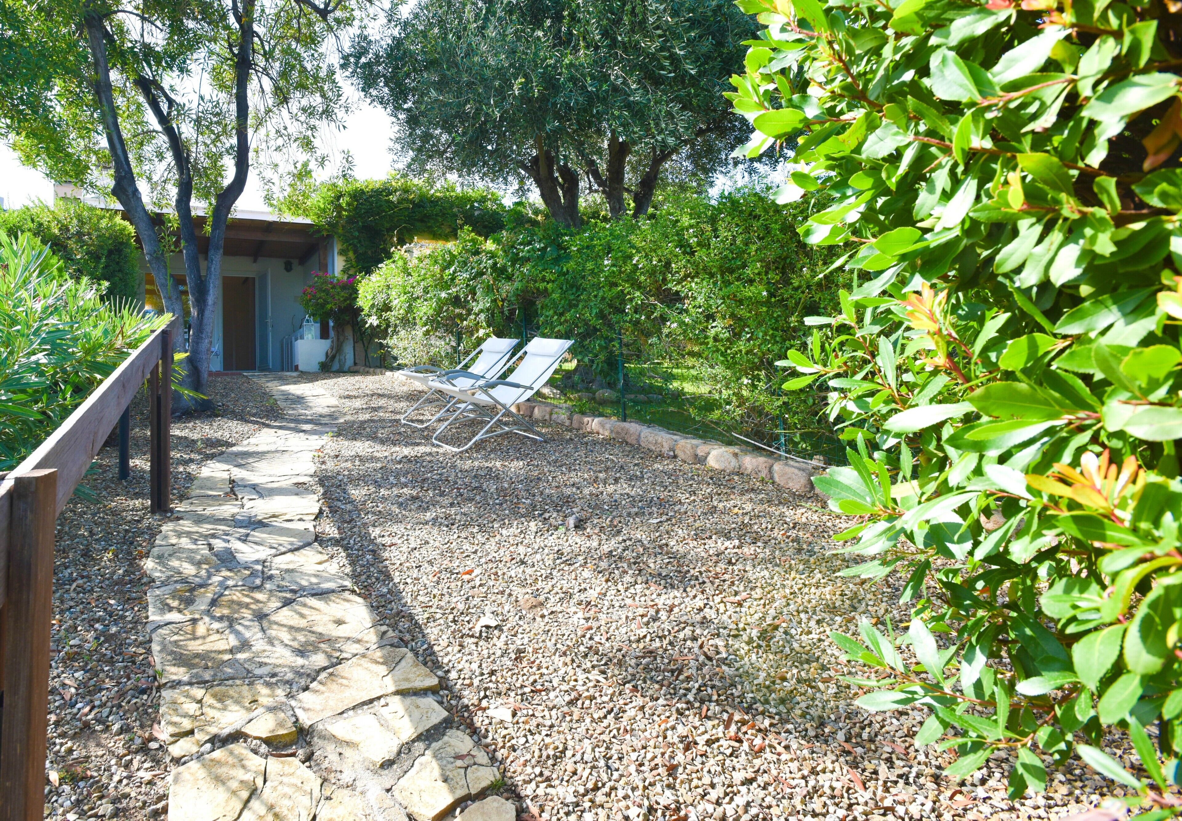A stone pathway leading to a seating area with two lounge chairs, surrounded by greenery and trees.