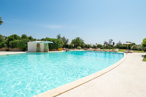 A swimming pool with lounge chairs and umbrellas, surrounded by greenery.