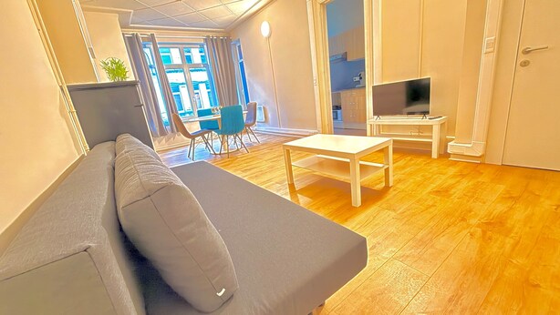 Ett modernt vardagsrum med en soffa, ett soffbord, ett TV-bord och en matplats med stolar.