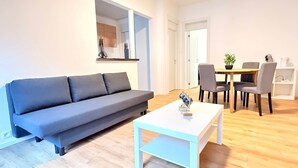 A modern living room with a grey sofa, a white coffee table, and a dining area with a table and chairs. - Orléans 41 (C) city center-train station-airport (Charleroi)