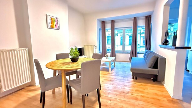 A modern living room with a dining area, a sofa, a TV, and a view of the city. - Orléans 41 (C) city center-train station-airport (Charleroi)
