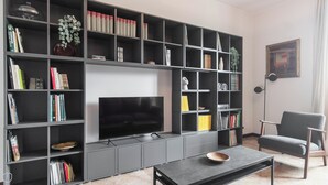 Un salon doté d’un grand téléviseur à écran plat, d’une bibliothèque remplie de livres, d’objets décoratifs et d’un fauteuil moderne.