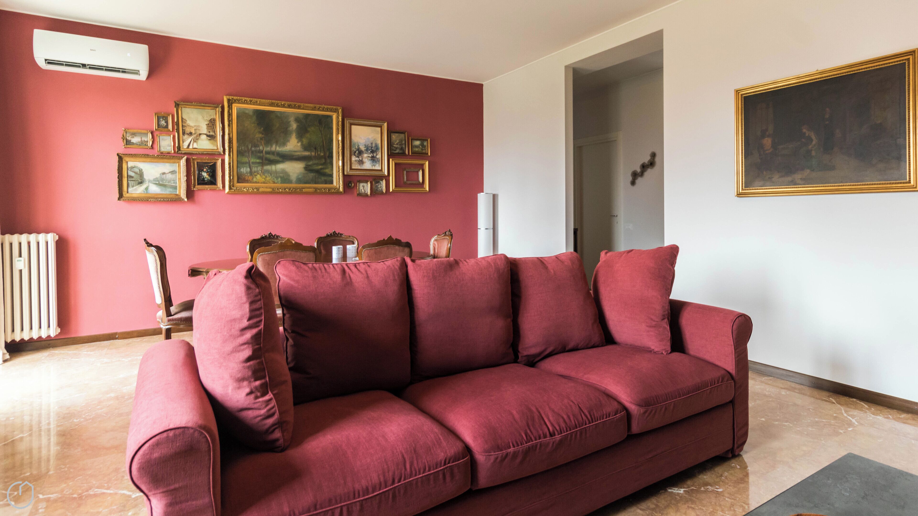 A living room with a red sofa, a dining table with chairs, and a wall with framed pictures.