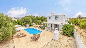 Eine moderne Villa mit Swimmingpool, Sitzgelegenheiten im Freien und üppiger Bepflanzung.