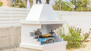 Ein weißer Grill für den Außenbereich mit Schornstein, ein Maiskolben auf dem Grill und ein weißer Zaun im Hintergrund.