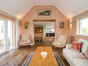 A spacious living room with a herringbone floor, a wooden coffee table, two armchairs, a sofa, and a dining area with a kitchen in the background. - Hoddell Pitch Cottage (Presteigne)