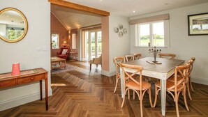 A dining area with a wooden herringbone floor, a round table with chairs, and a large mirror on the wall. - Hoddell Pitch Cottage (Presteigne)