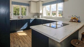 A modern kitchen with dark blue cabinets, a large island, and pendant lighting. - Hoddell Pitch Cottage (Presteigne)