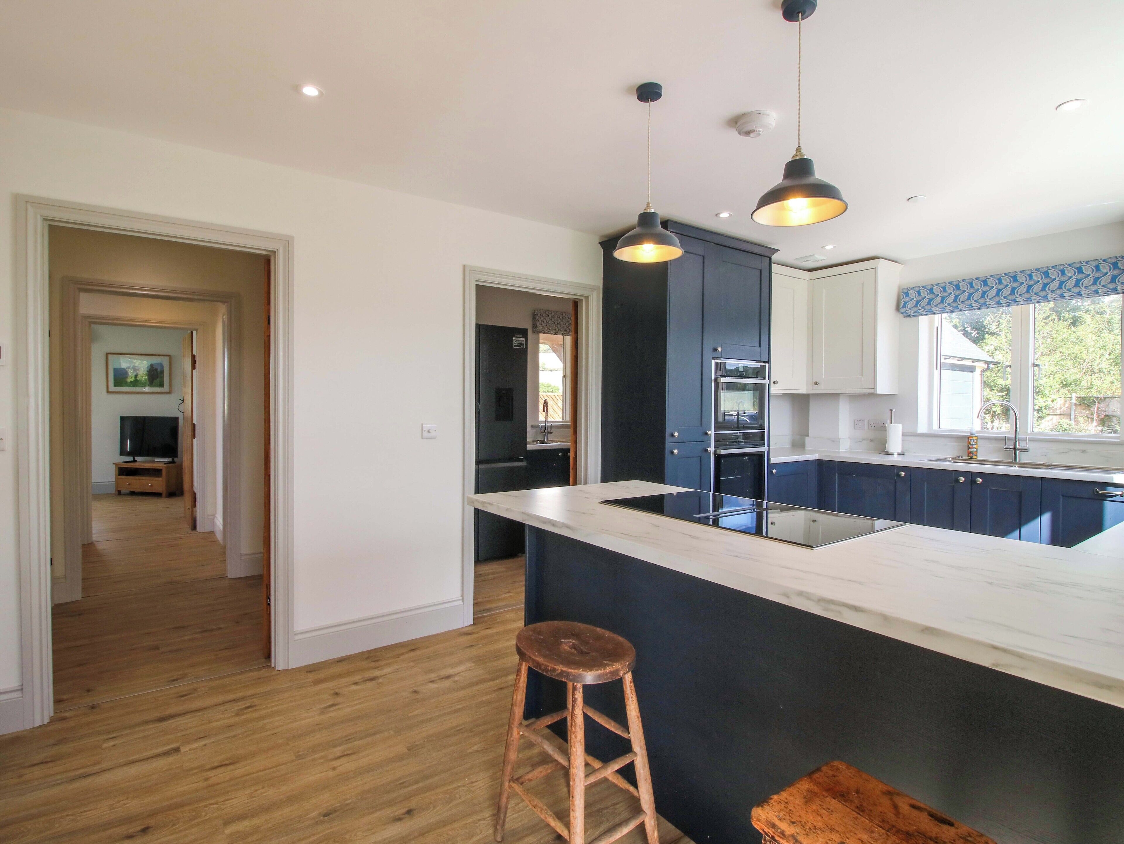 A modern kitchen with dark blue cabinets, a white countertop, and a wooden stool.