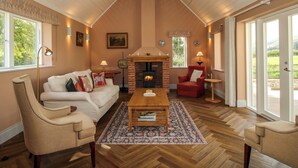 A cozy living room with a fireplace, a sofa, a red armchair, and a coffee table. - Hoddell Pitch Cottage (Presteigne)