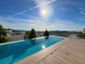 Una piscina infinita en la azotea, con vistas despejadas a un horizonte urbano y montañas a lo lejos.