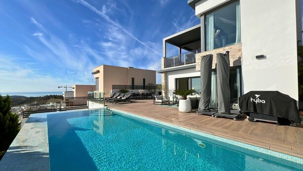 Un área de piscina moderna con una piscina azul cristalina, sillas de descanso y una parrilla.