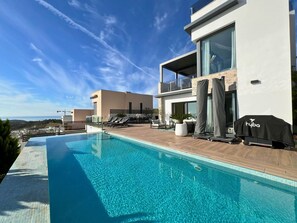 Un espace piscine moderne avec une piscine à l’eau cristalline, des chaises longues et un barbecue.