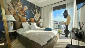 Una habitación de hotel moderna con una cama grande, dos mesitas de noche, un gran ventanal con vistas y un mural decorativo en la pared.