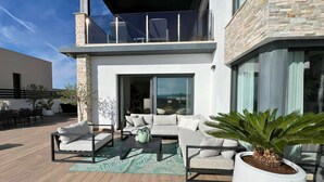 Un espacio exterior moderno con un conjunto de sofás, una mesa de comedor y plantas en macetas.