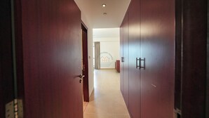 Een gang met houten deuren en een betegelde vloer, die leidt naar een kamer met een bed en een raam.