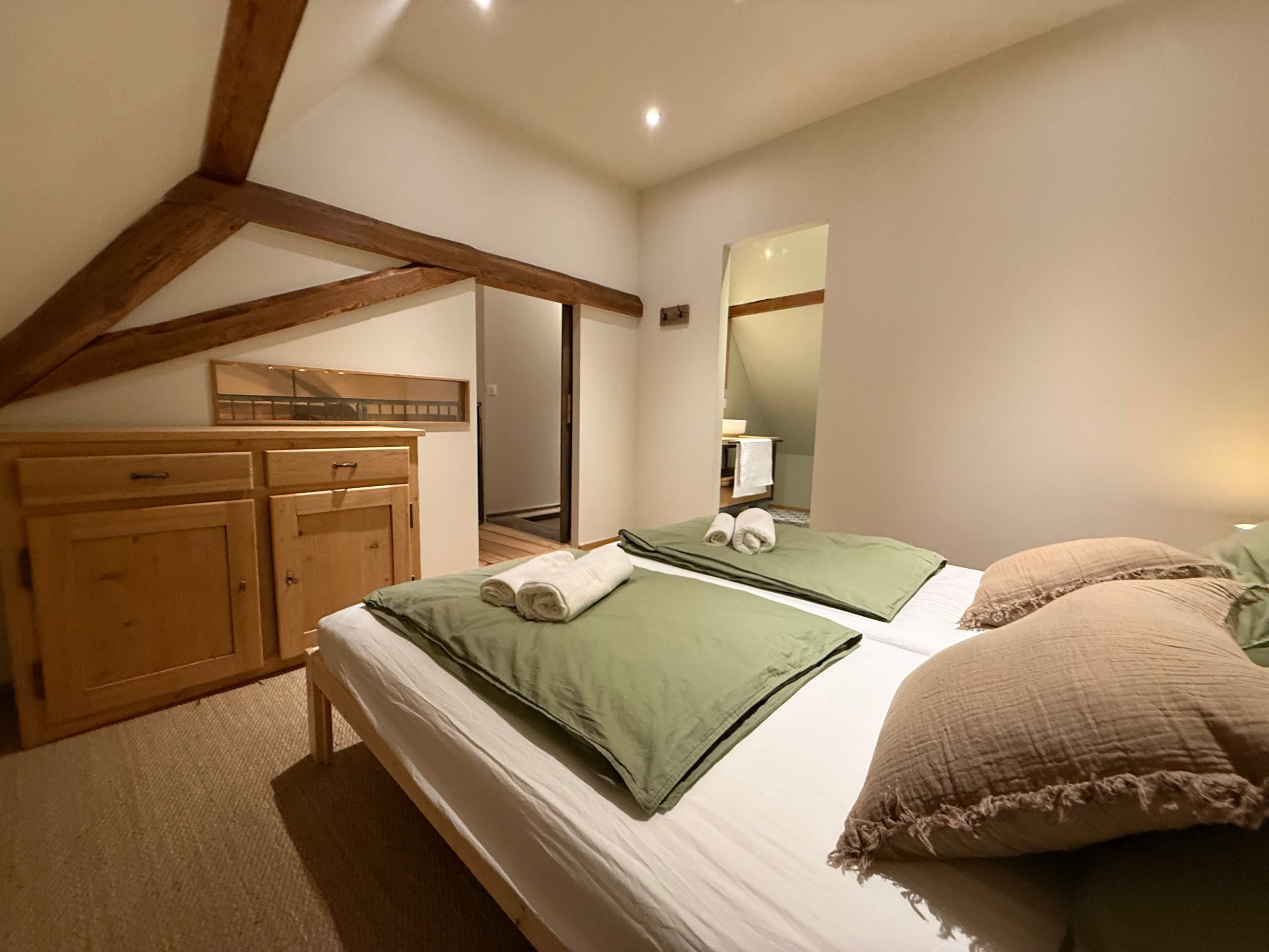 A bedroom with a wooden wardrobe, a bed with green and beige bedding, and a mirror on the wall.