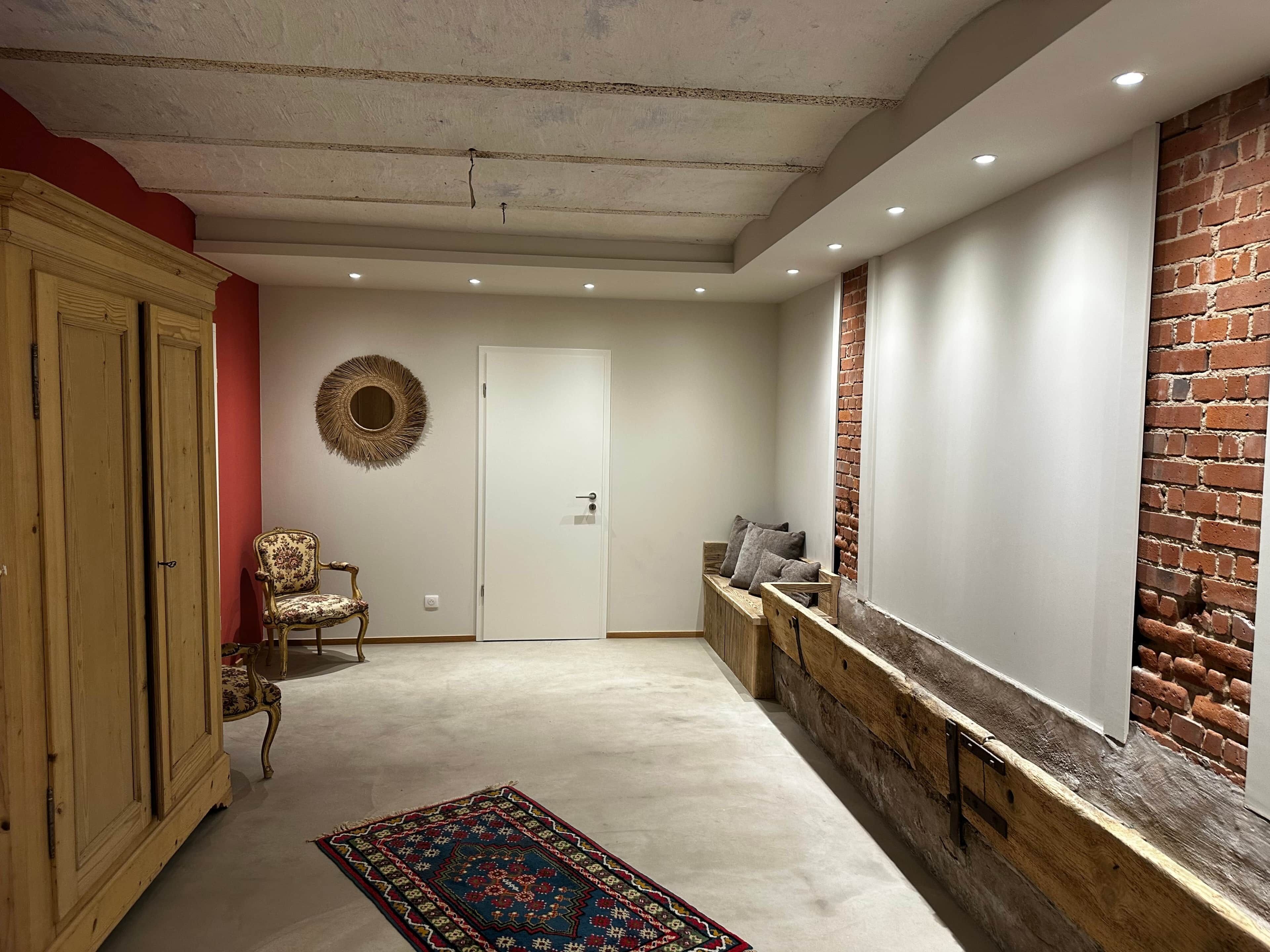 A hallway with a patterned rug, a wooden bench with cushions, a decorative mirror, and a door.