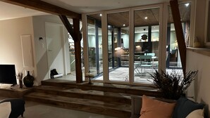 A modern living room with a sofa, a coffee table, and a TV. There is a staircase leading to a balcony with glass doors. - L'Étable - at the Ancienne ferme (Steinseltz)