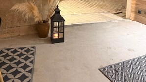 A rustic room with a concrete floor, a patterned rug, pampas grass in a vase, and a lantern. - L'Étable - at the Ancienne ferme (Steinseltz)